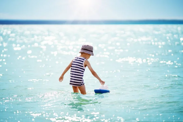 Cute boy gry z zabawką statku w wodzie na morzu. — Zdjęcie stockowe