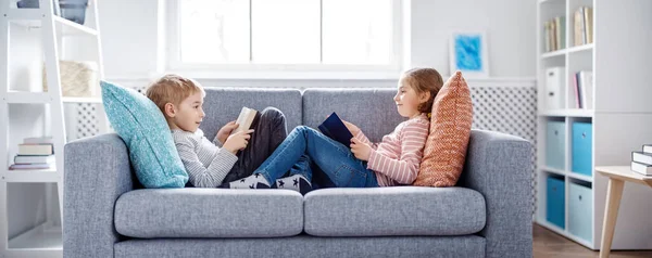 Leuke kinderen zittend op de zachte bank en leesboeken — Stockfoto