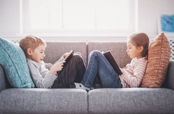 Yumuşak kanepede oturup kitap okuyan sevimli çocuklar. — Stok fotoğraf