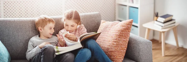 Leuke kinderen zittend op de zachte bank en leesboeken — Stockfoto