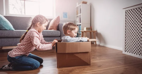 Bonito crianças brincando com caixa de papelão na sala de estar. — Fotografia de Stock