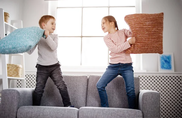 Leuke kinderen vechten door kussens op de bank — Stockfoto