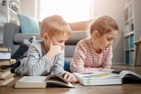 Tatlı çocuklar yere yatıp kitap okuyorlar. — Stok fotoğraf