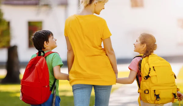 Mor går med son och dotter på skolgården. — Stockfoto