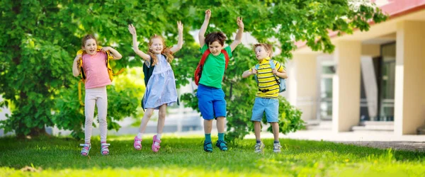 Söta barn med ryggsäckar hoppar och leker i parken nära skolan — Stockfoto