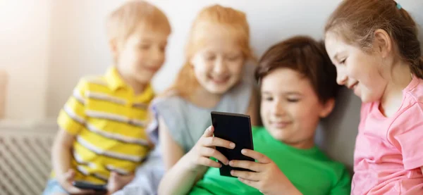 Група дітей, які сидять в приміщенні і дивляться в смартфон — стокове фото