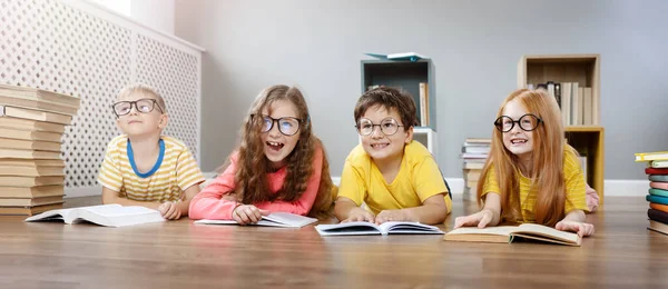 Vier schattige kinderen in bril liggend op de vloer binnen met boeken — Stockfoto