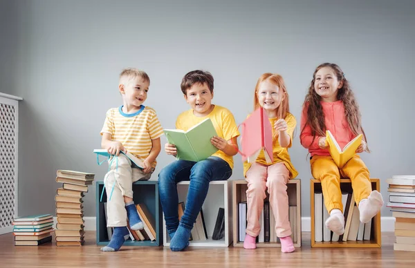Группа детей, сидящих на книжных стопках и на книжных полках в комнате и читающих периодически. — стоковое фото