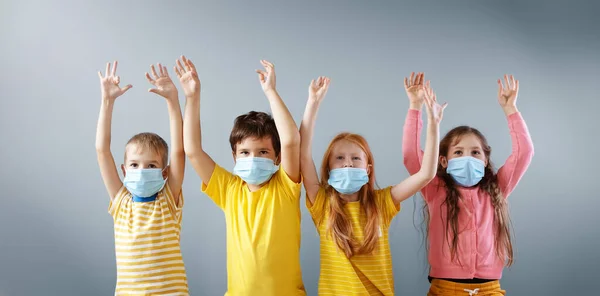 Grupo de quatro crianças em máscara médica em pé dentro de casa com as mãos erguidas. — Fotografia de Stock