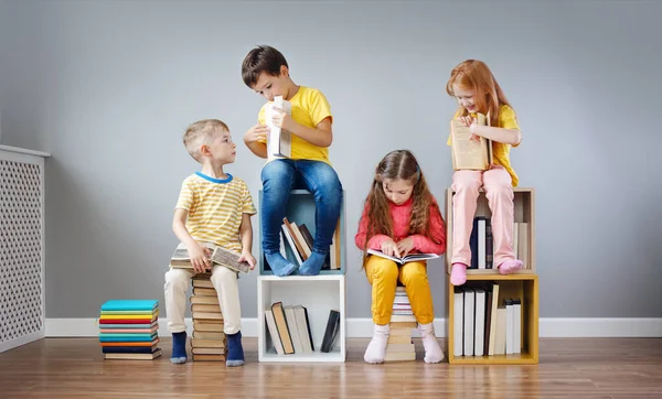 Gyerekek csoportja ül a könyvespolcokon és a könyvespolcokon a szobában és olvas időszakosan. — Stock Fotó