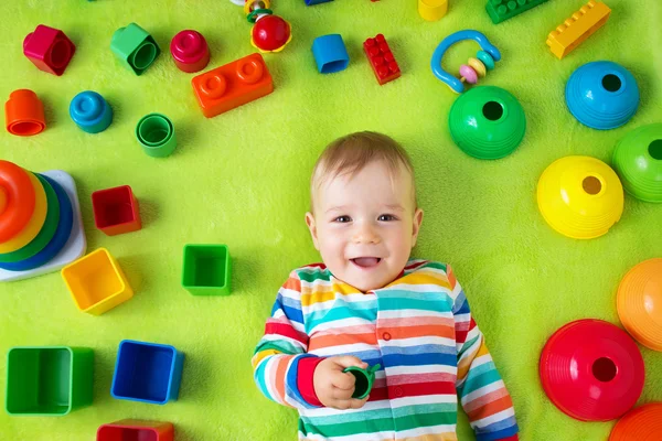 Menino deitado no cobertor com muitos brinquedos ao redor — Fotografia de Stock