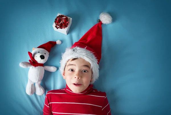 Щасливий хлопчик у капелюсі Санта Клауса з білим ведмедем на синьому фоні — стокове фото