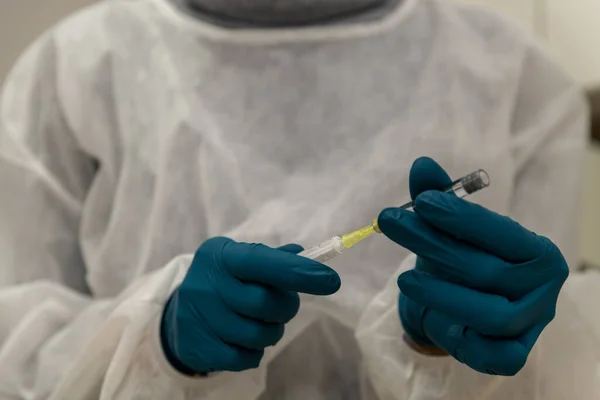 Doctor filling syringe with Corona vaccine, Covid-19, hands in rubber gloves and white coat, close up.