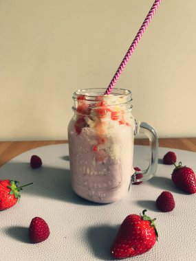 Çilekli meyve suyu bardakta, çilek ve ahududuyla süslenmiş..