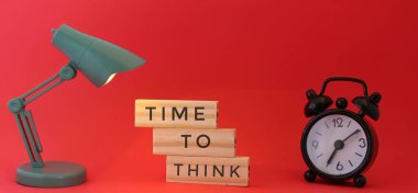 Masa lambasının seçici odak görüntüsü, alarm saati ve ahşap kiremitlere yazılmış düşünme zamanı.