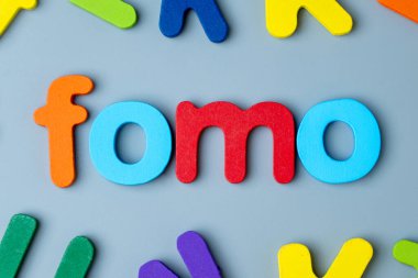 FOMO kelimesini oluşturmak için düzenlenmiş renkli ahşap alfabe harfleri. Kaçırma korkusu, dijital endişe, sosyal baskı konsepti.