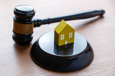 Küçük sarı bir ev modeli ve yargıç tokmağı. Emlak hukuku, mülkiyet hakları, haciz konsepti.