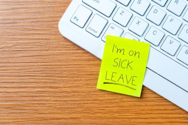 Bilgisayarın klavyesine el yazısıyla yazılmış hasta bir mesaj bırakılmış. Çalışan yokluğu, işyeri politikası ve tıbbi izin kavramı.