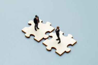 Minyatür iş figürleri birbirine kenetlenmiş yapboz parçaları üzerinde duruyor. Şirket ortaklığı, takım çalışması, stratejik işbirliği konsepti.