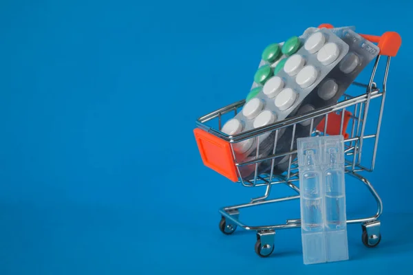 Concept of online shopping, ordering and delivery of medicines. Blister packs of medicines in a shopping trolley on a blue background.