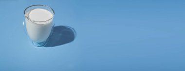 glass of milk on a blue background. hard shadows. World Milk Day. vegetable or animal milk. healthy eating.banner