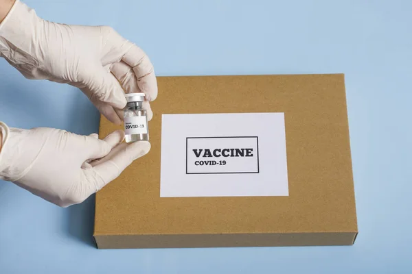 Coronavirus aşısı içeren tıbbi konsept kutusu. Beyaz eldivenli bir doktorun elinde mavi arka planda bir şişe covid 19 aşı ya da ilaç bulunur..