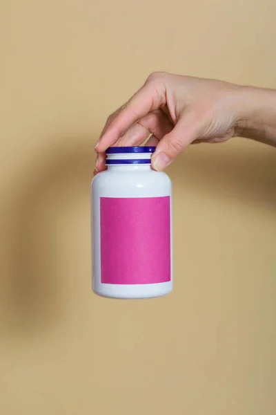 yakın plan, bej arka plan. Kız elinde beyaz bir şişede vitamin tutuyor. Bağışıklık ve iyileşme için vitaminler. Güzellik için vitaminler. mesaj için yer. dikey resim