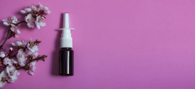 Burun spreyi ve pembe arka planda çiçek açan dal örneği. Alerji ilacı. Bayrak.