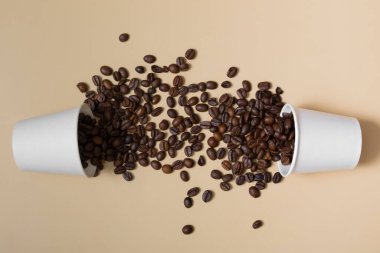 Bej arkaplanda kahve çekirdekleri olan beyaz bardakları taklit et. İki kağıt bardak.