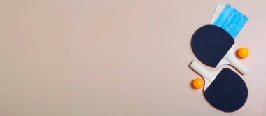 Tenis raketleri, top ve bej arka planda tıbbi maskeler. Karantina ve pandemik süresince açık hava eğlencesi.