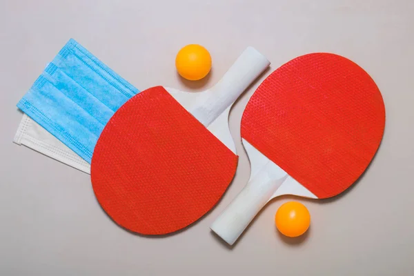 Tenis raketleri, top ve bej arka planda tıbbi maskeler. Karantina ve salgın sırasında açık hava eğlencesi.