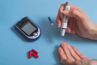 Kadın kan şekerini tutkalla ölçer. Mavi arka planda şeker hastalığı konsepti.