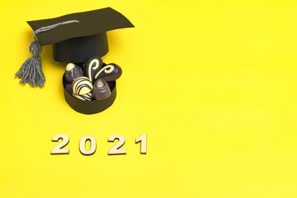 A box of chocolates in the form of a graduate hat. Chocolate day concept. Graduation 2021 on colored background