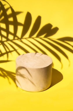 Minimalistic stone podium on yellow background shaded by palm leaves for product display