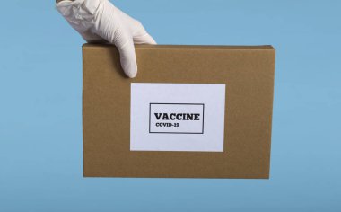 Tıbbi eldivenli bir tıp uzmanının elinde mavi arka planda izole edilmiş bir kutu kovid19 aşısı var.