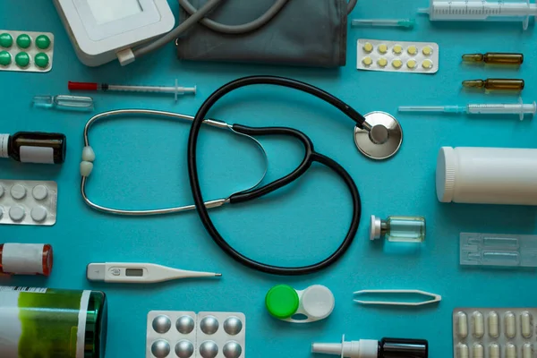 Üst görünüm medikal düzlem: stetoskop, termometre, şırınga, haplar, sprey, mavi arka planda lensler - üst görünüm düz model
