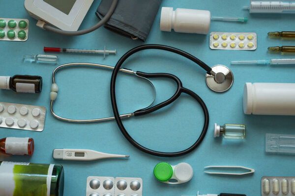 Top view medical flat layout: stethoscope, thermometer, syringe, pills, spray, lenses on blue background - top view flat mockup