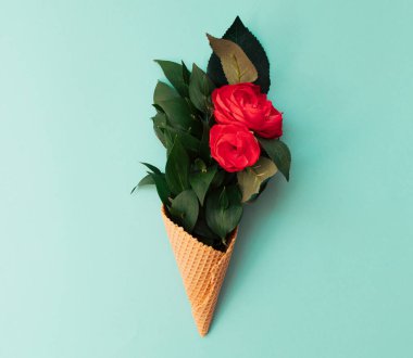 Dondurma külahında çiçek buketi. İlham için yaratıcı bir kavram. Mavi arka planda kırmızı güller ve yeşil yapraklar.