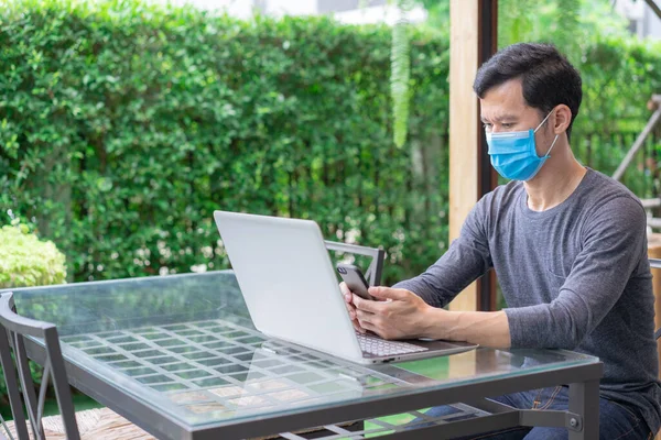 Ung Man Medicinsk Ansiktsmask Med Hjälp Smarttelefon Sms Medan Arbetar Stockbild