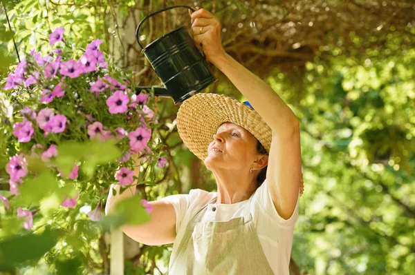 Старша жінка поливає квіти у висячому горщику — стокове фото