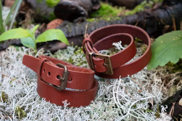 two brown leather bracelet close up on blurred green moss and grass in the forest