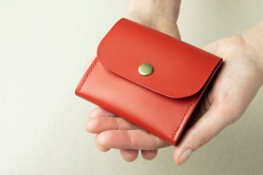 bright red leather wallet in open female hands close-up on a gray background