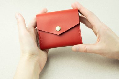 bright red leather wallet in female hands close-up on a gray background