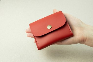 red leather wallet in a woman's hand close-up on a gray background with shadows