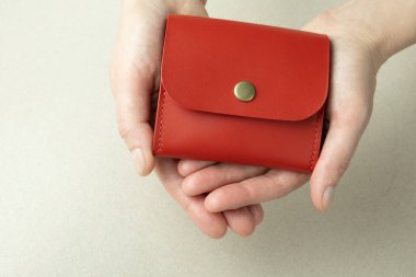 red leather wallet in open female hands close-up on a gray background