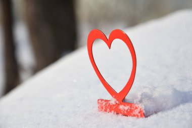 Canlı kırmızı şamdanın görüntüsü kalp şeklinde kışın yumuşak kar üzerinde güneş ışığında bulanık arkaplanda. 