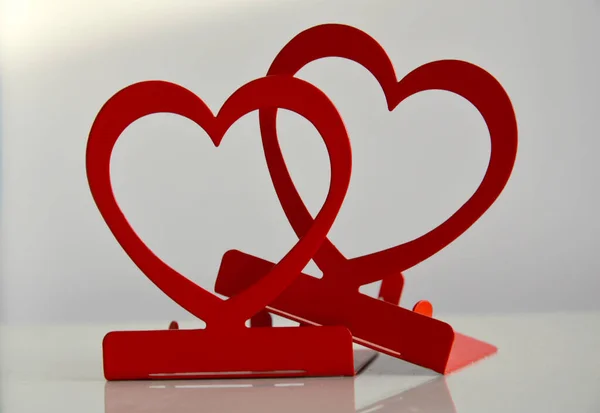 Kırmızı şamdanların yakın çekim şekli beyaz parlak masa üzerindeki kalplerin üzerinde gün ışığında bulanık arka planda. 