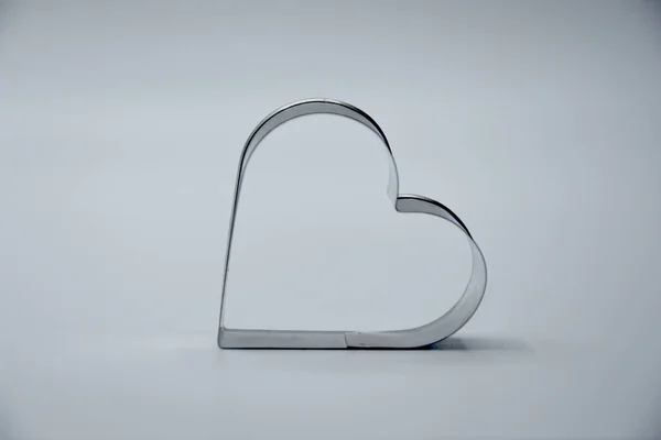 Beyaz arka plandaki lambalar ışığında kalp şeklinde küçük gri metalik kurabiye kesicinin yakın plan görüntüsü 