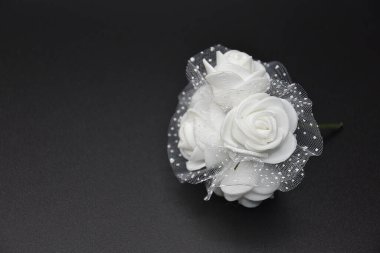 Siyah arka plandaki lamba ışığında şeffaf kumaş örtüsüyle çevrili küçük, narin, kırılgan beyaz çiçeklerin seçici odağı. 