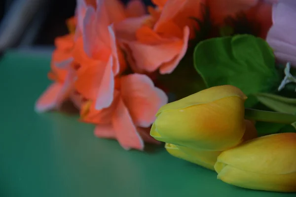 Gün ışığında yeşil masanın üzerinde küçük ince yapraklı, canlı, çok renkli, yapay çiçeklerin olduğu bir buket. 